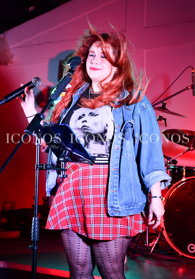 Ella Rockwell performing at Alianza Francesa in San Pedro Sula, with a vibrant rock atmosphere, wearing a denim jacket and plaid skirt.